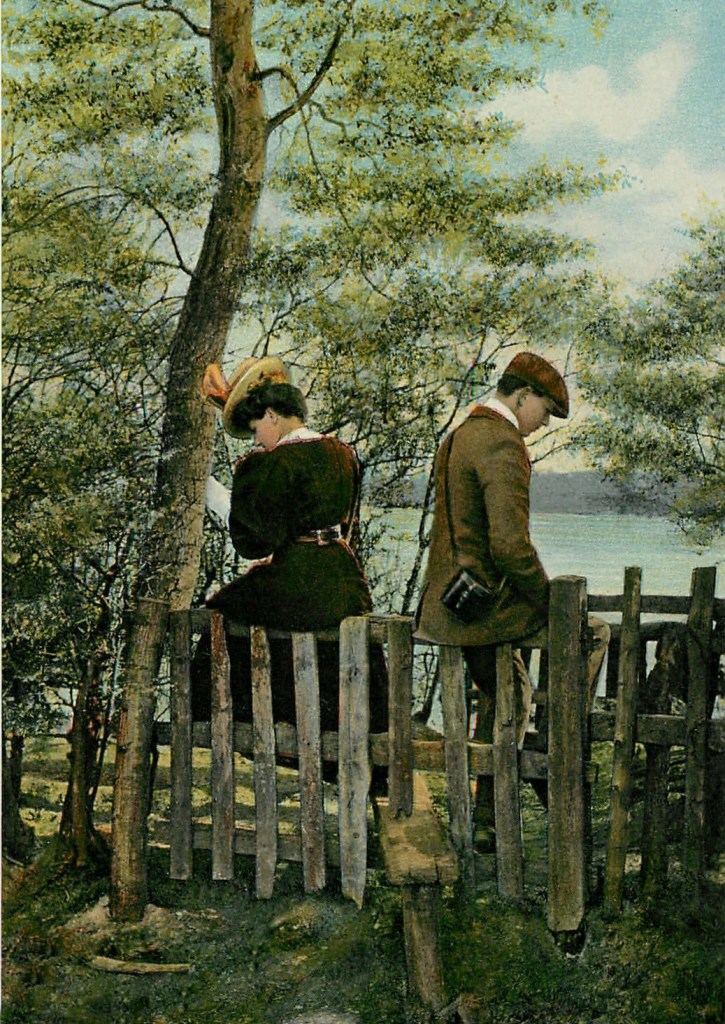 A young couple sits outside on a fence rail, facing away from each other as if they have had a disagreement.