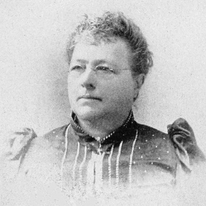 Black and white head-and-shoulders photograph of Emma P. Ewing. She is wearing spectacles. She is wearing a bodice with a high neck and sleeves that puff at the shoulder. 