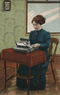 Old hand-colored photograph of a woman about 1915 wearing a blue dress with long-sleeves, high neckline, and floor-length skirt. she is seated at a small table on which is a red tablecloth and a typewriter.