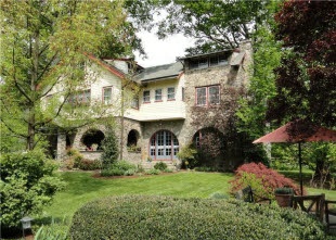 Photograph of a large two-story home with brick accents set back from the street with lush green lawns and mature trees.