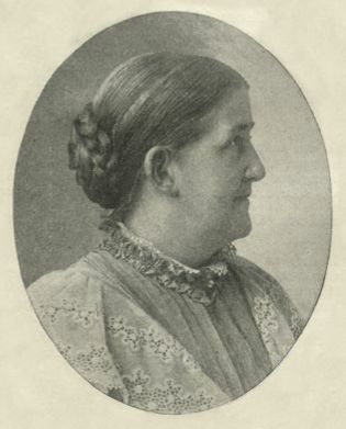 Black and white photo of Isabella Alden in profile, showing her hair parted in the middle and combed back into a braided bun at the back of her head.