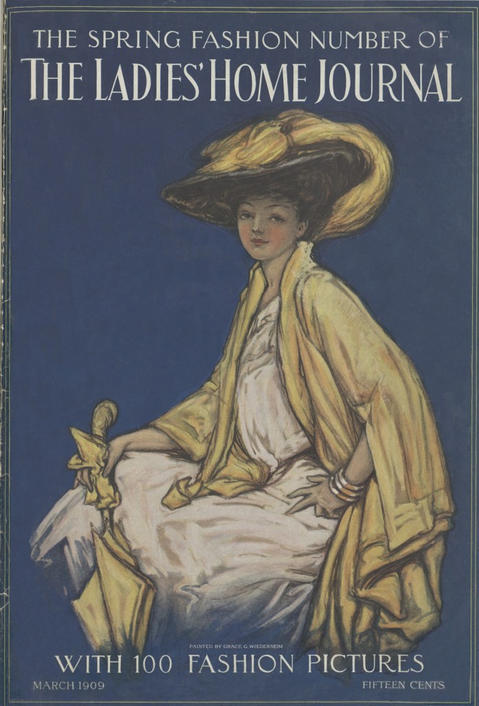 Cover of The Ladies' Home Journal magazine. The color illustration shows a stylish young woman seated, wearing a white dress. A gold colored cape is drawn open with one of her hands. In the other hand she holds a matching pair of gloves and an umbrella. On her head is a wide-brimmed hat fashionable in 1909. Covering the brim of the hat and cascading over the brim at the back is an arrangement of feathers dyed gold to match her outfit.